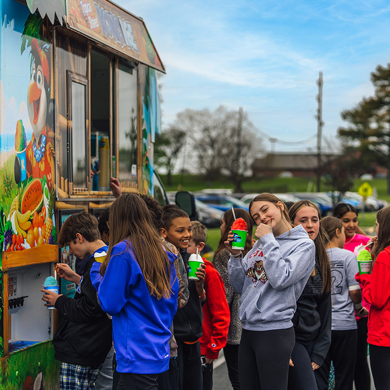 A group of students waits in line at a Kona Ice truck for a school event